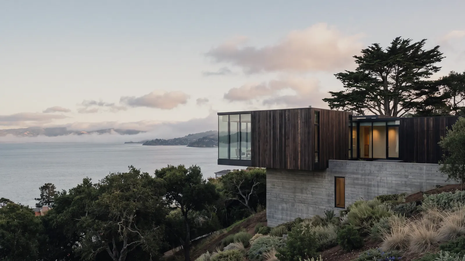 A modern wood and concrete home on a hillside above the water