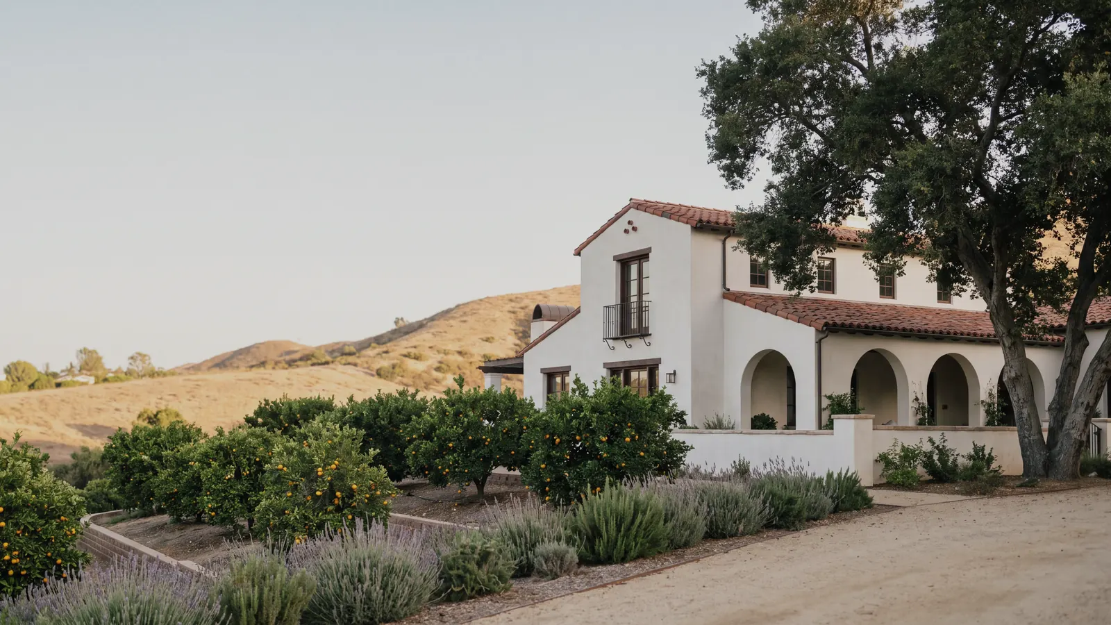 A white Spanish-style home with arched windows and a tile roof in the hills