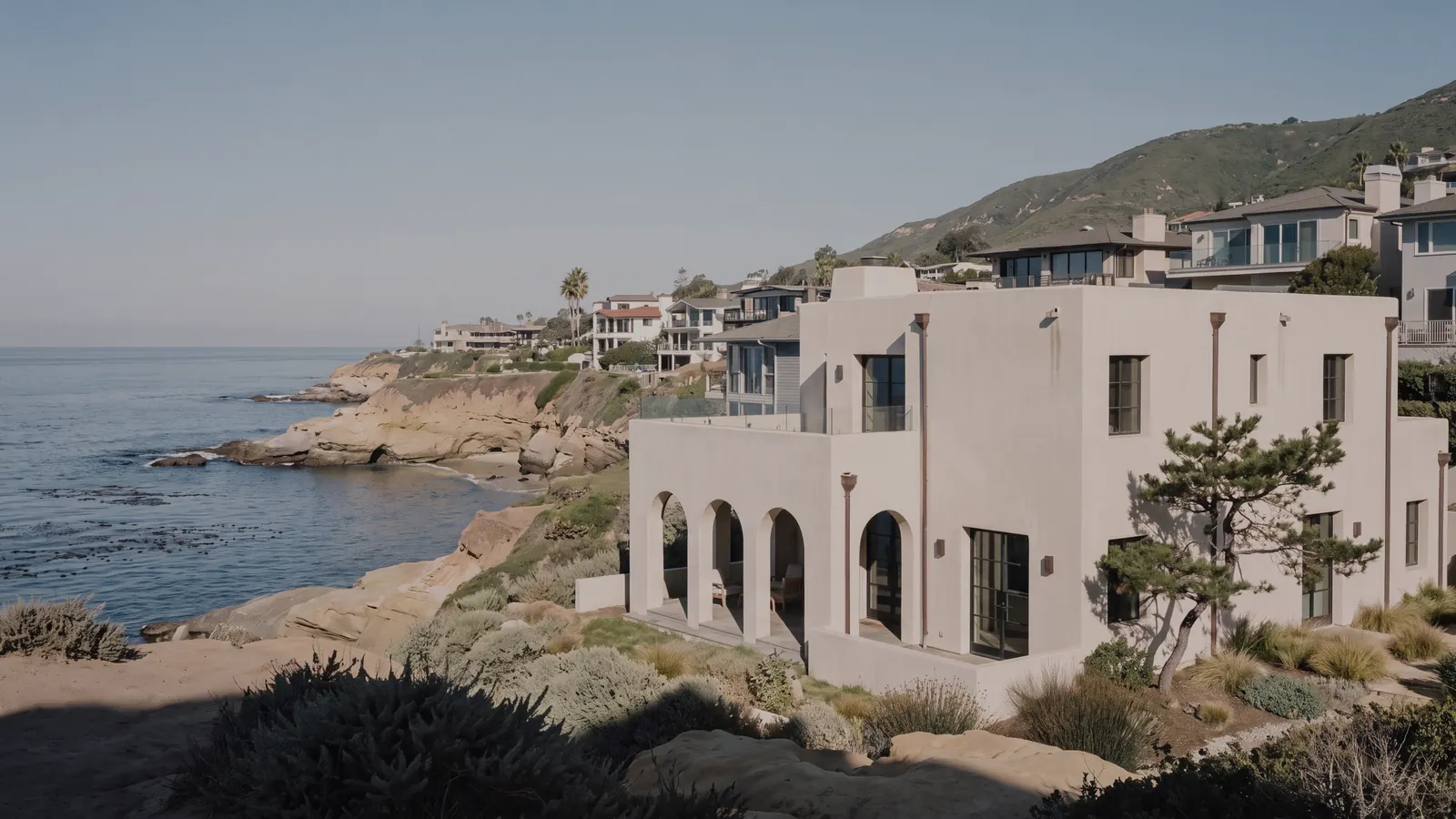 A white home with arched windows on a cliff above the ocean